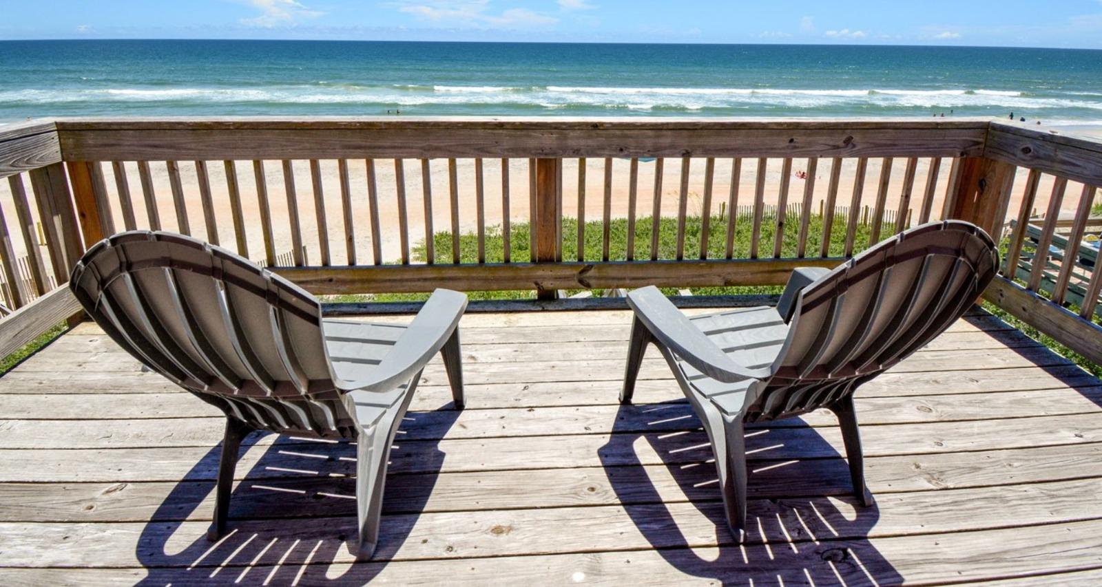 Two adirondack chairs on a wooden deck overlooking the ocean at a Surf City vacation rental.